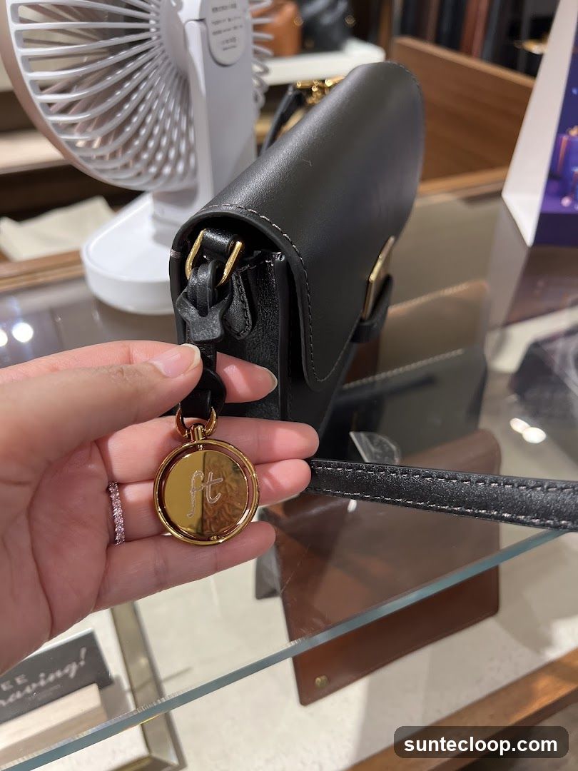 Hand holding a black handbag with a gold charm