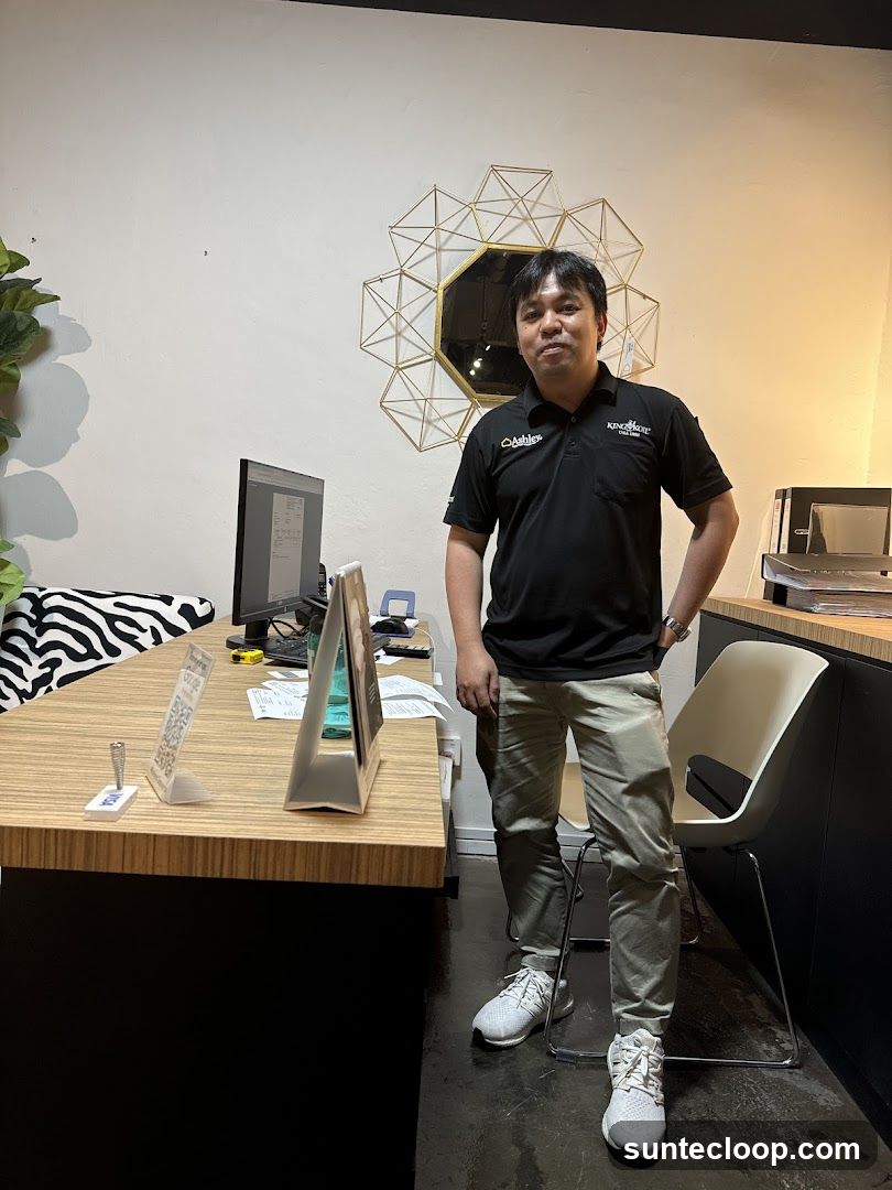 Man in a black polo shirt and khaki pants standing behind a desk
