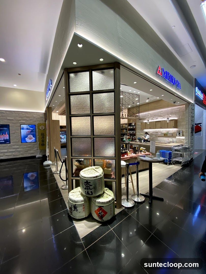 A well-lit storefront with the name MEIDI-YA displayed prominently in blue neon letters above the entrance. The shop features a modern design with frosted glass panels and a clean interior visible through the open doorway. Several large, decorative barrels are stacked outside the entrance, adding a traditional touch. The floor is highly reflective black tile.