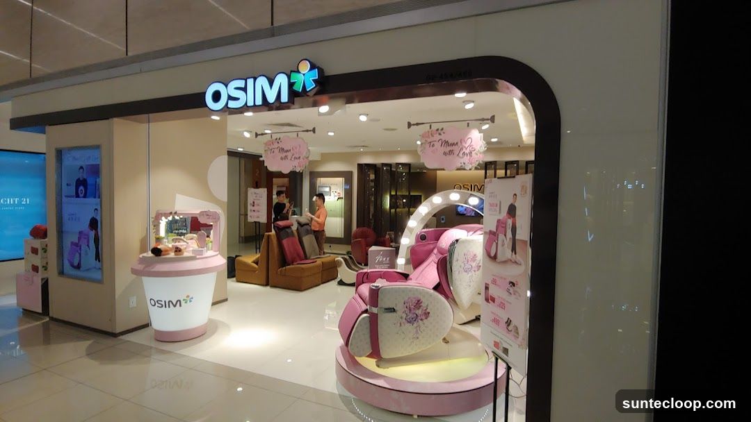 The exterior of an OSIM store with its prominent logo above the entrance. Inside, massage chairs and other products are displayed, with staff attending to customers. Decorative signs with floral motifs and the text "To Mama with Love" are hung.