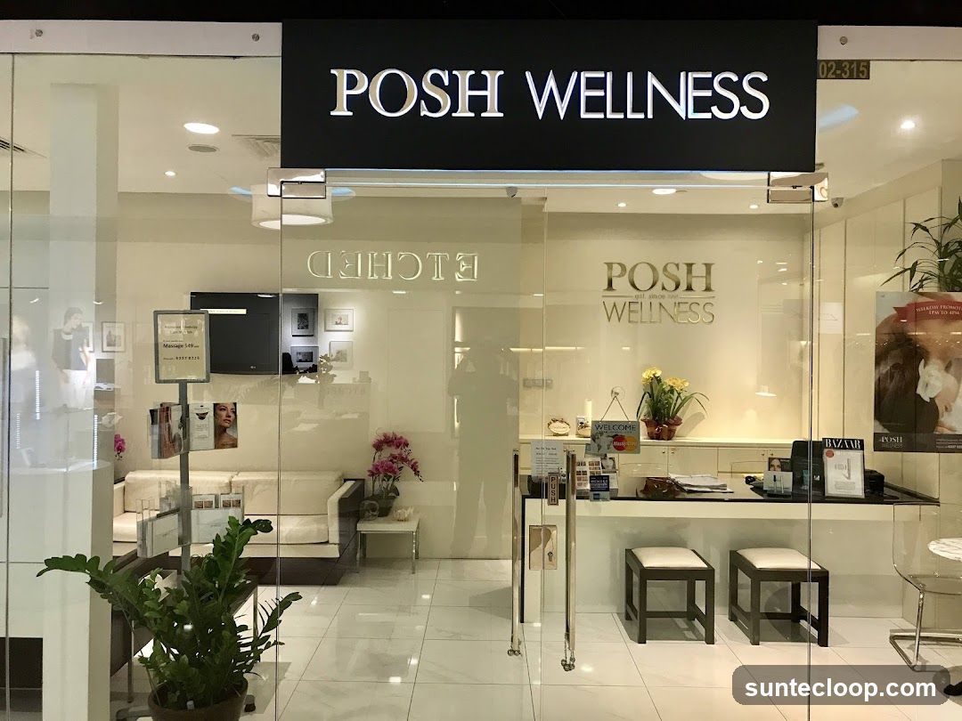 The exterior of a Posh Wellness establishment with a large glass facade. A prominent sign above the entrance reads "POSH WELLNESS". Inside, a reception desk is visible with two stools, a sofa, and plants. Promotional materials and artwork are displayed on the walls and on stands.
