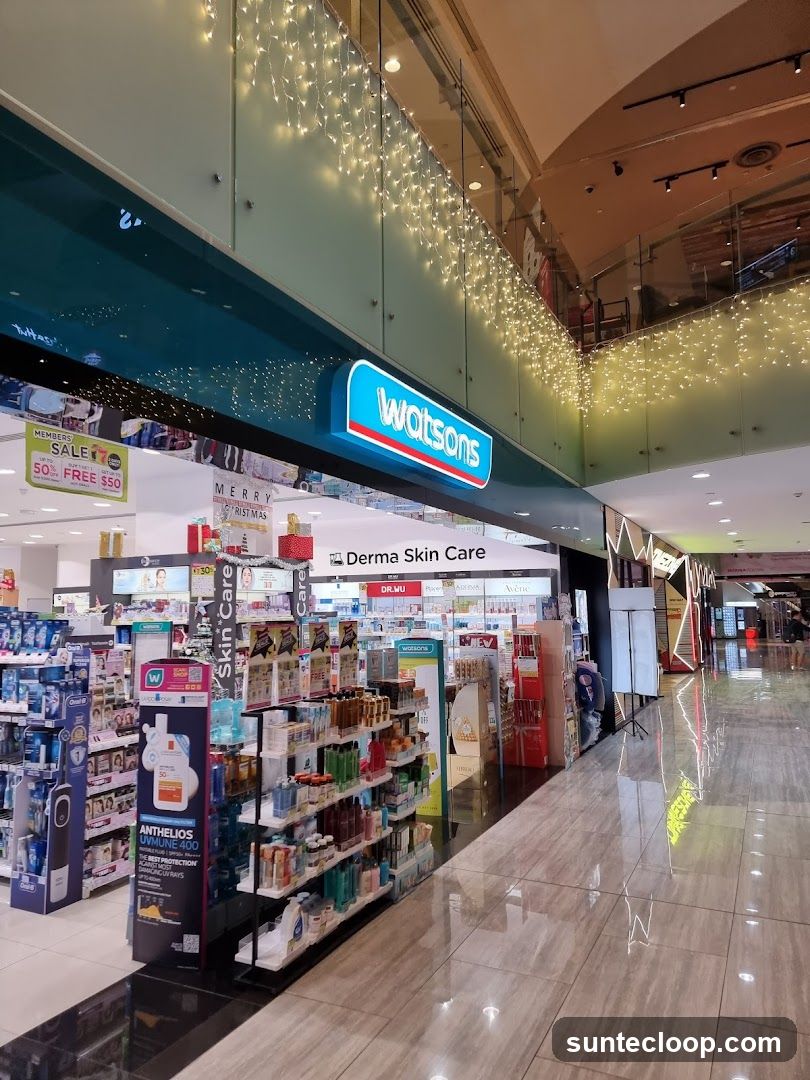 The exterior of a Watsons store, decorated with festive lights. Shelves stocked with various skincare and health products are visible inside. A sign above the entrance reads "Watsons" and "Derma Skin Care". Promotional signs for a sale are also displayed.
