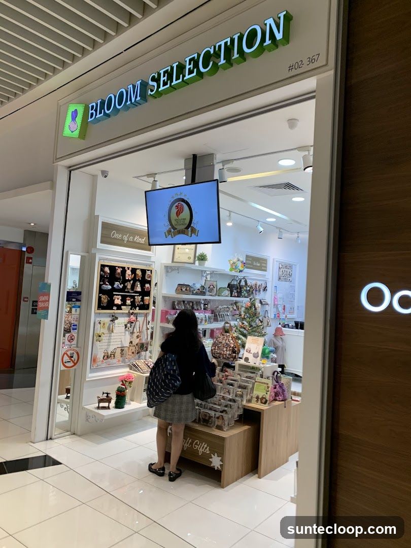 The exterior of a shop called Bloom Selection. The shop sells various items including bags, accessories, and decorative items. A woman is browsing the merchandise inside the shop.