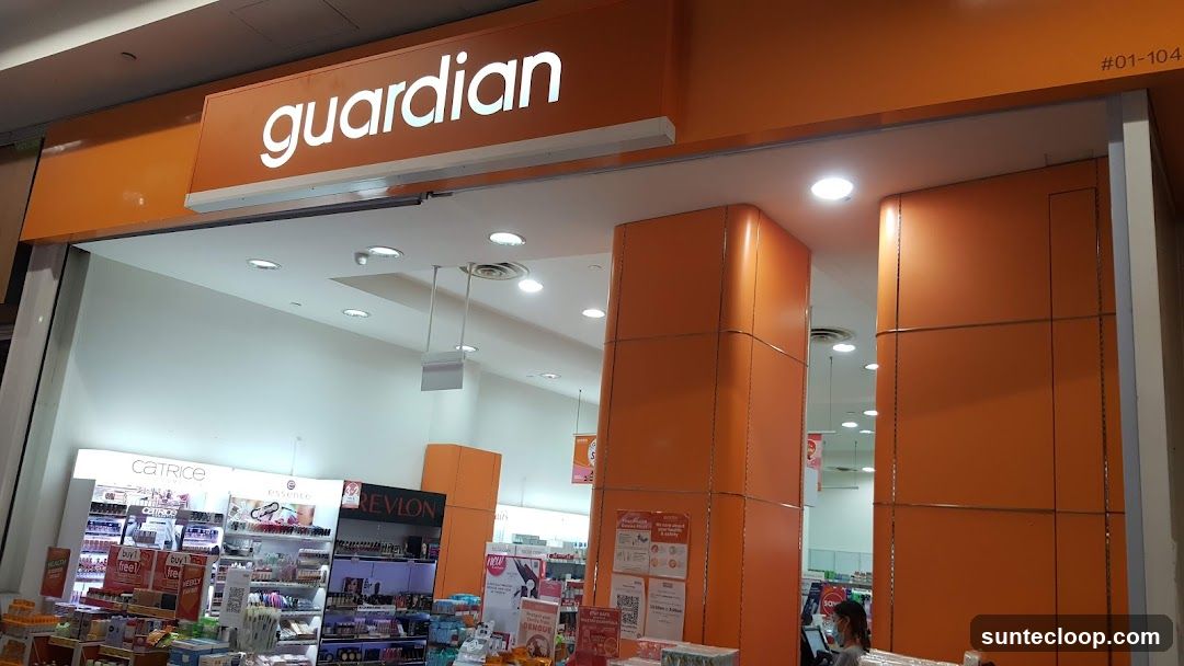 The exterior of a Guardian store with its prominent orange and white signage. The entrance is visible, leading into a well-lit interior stocked with various beauty and health products. Brands like Catrice, Essence, and Revlon are displayed on shelves.
